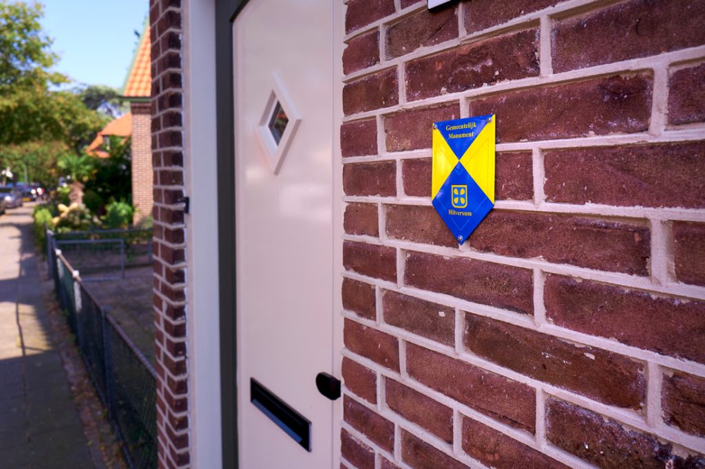 Naast de voordeur van een woning in de Bloemenbuurt in Hilversum hangt een monumentenschildje aan de gevel.